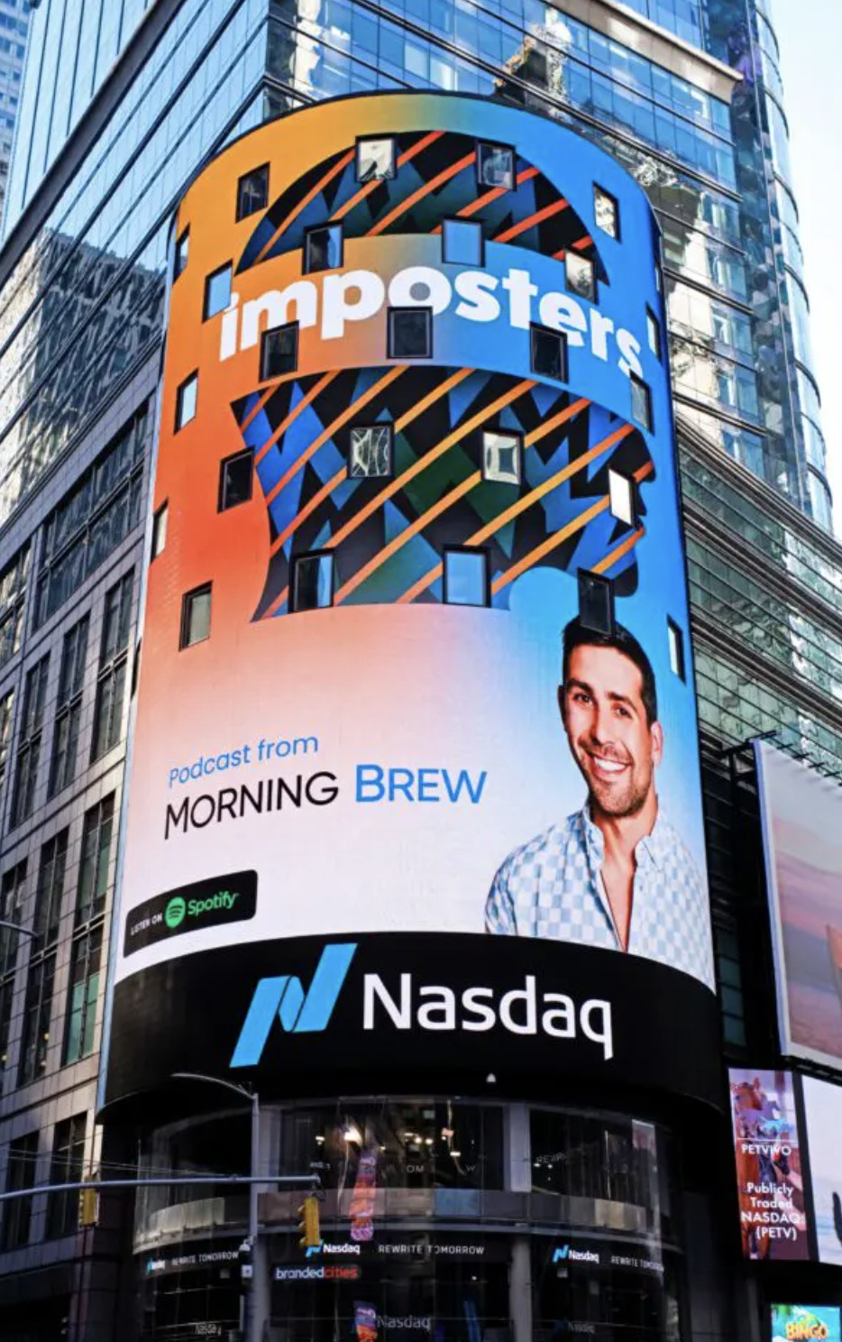 Nasdaq billboard in Times Square promoting the 'Imposters' podcast from Morning Brew, with a colorful background and host’s image.