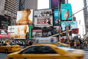 Times Square billboards with a School of Rock ad and yellow cabs passing by.